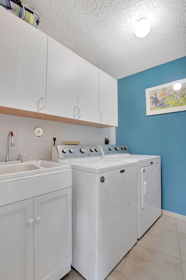 laundry area with light tile patterned flooring, sink, cabinets, washing machine and clothes dryer, and a textured ceiling