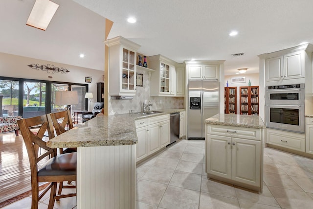 kitchen with appliances with stainless steel finishes, backsplash, a kitchen bar, light stone counters, and kitchen peninsula