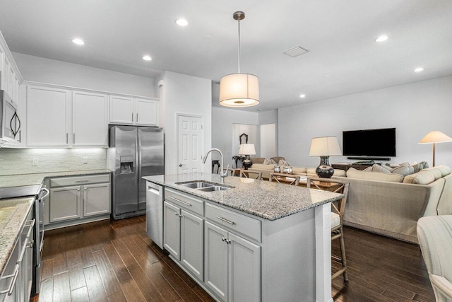 kitchen featuring dark wood-type flooring, sink, decorative light fixtures, appliances with stainless steel finishes, and a kitchen island with sink