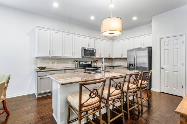 kitchen with sink, white cabinetry, stainless steel appliances, light stone countertops, and a kitchen island with sink