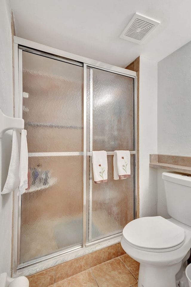 bathroom featuring tile patterned floors, toilet, and a shower with shower door