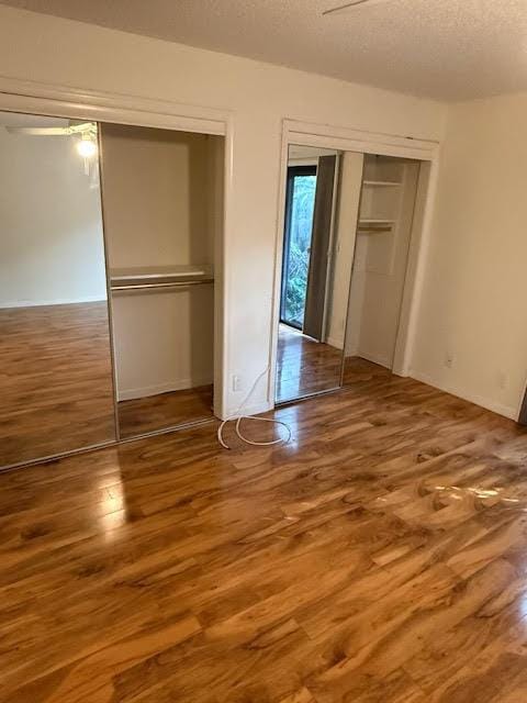 unfurnished bedroom featuring hardwood / wood-style floors, ceiling fan, multiple closets, and a textured ceiling