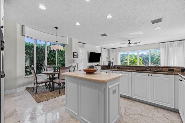 kitchen with sink, ceiling fan, white cabinets, a kitchen island, and decorative light fixtures