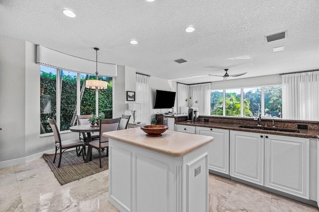 kitchen featuring pendant lighting, sink, ceiling fan, a center island, and white cabinets