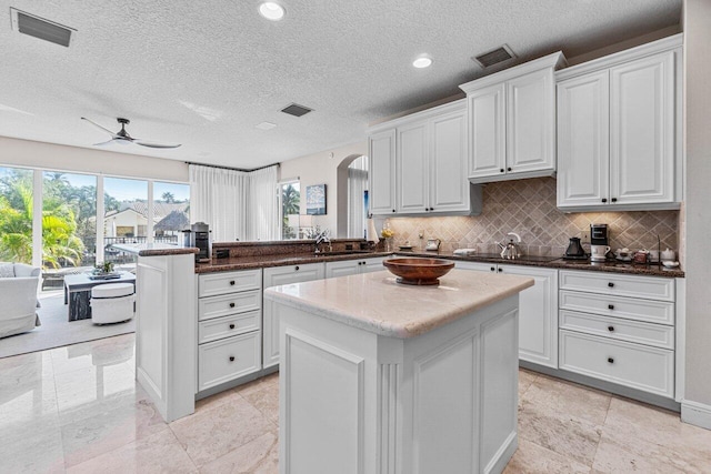 kitchen featuring white cabinetry, kitchen peninsula, a kitchen island, ceiling fan, and decorative backsplash