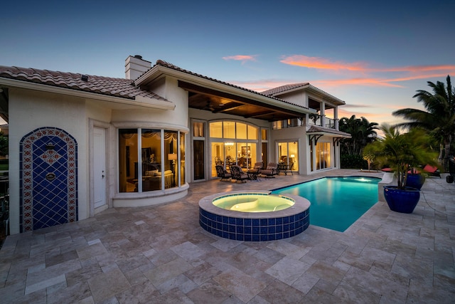 pool at dusk with an in ground hot tub and a patio