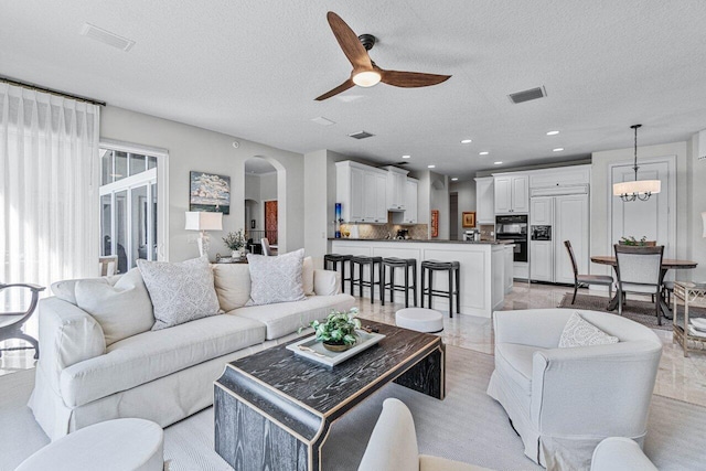 living room with ceiling fan with notable chandelier and a textured ceiling