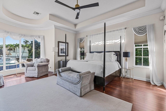 bedroom with a tray ceiling, dark wood-type flooring, ornamental molding, and ceiling fan