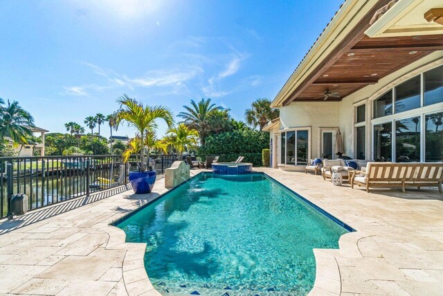 view of pool with ceiling fan, outdoor lounge area, a water view, a patio area, and an in ground hot tub