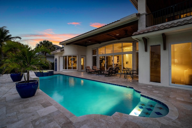 pool at dusk with an in ground hot tub and a patio