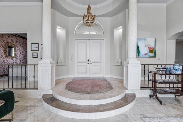 foyer entrance featuring an inviting chandelier, ornamental molding, decorative columns, and a high ceiling