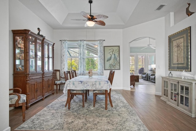 dining area with ceiling fan, a tray ceiling, and dark hardwood / wood-style flooring