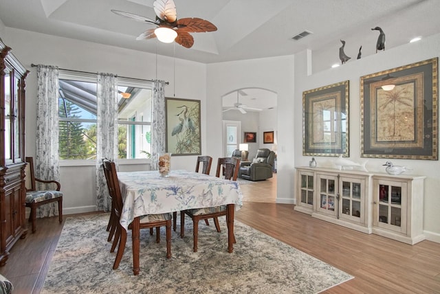 dining room with ceiling fan, a raised ceiling, and light hardwood / wood-style flooring