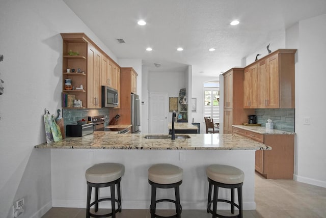 kitchen featuring sink, stainless steel appliances, light stone countertops, decorative backsplash, and kitchen peninsula