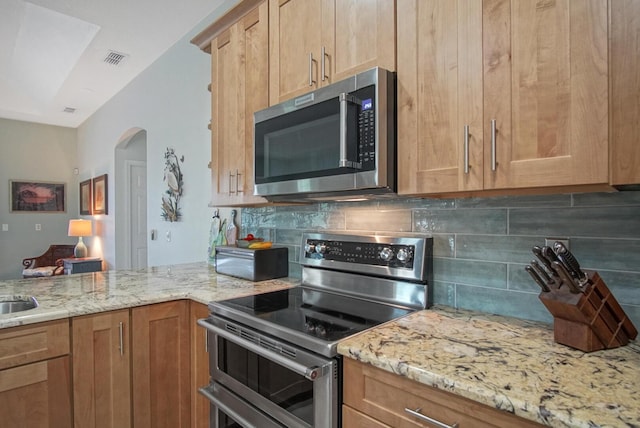 kitchen with tasteful backsplash, light stone countertops, and appliances with stainless steel finishes