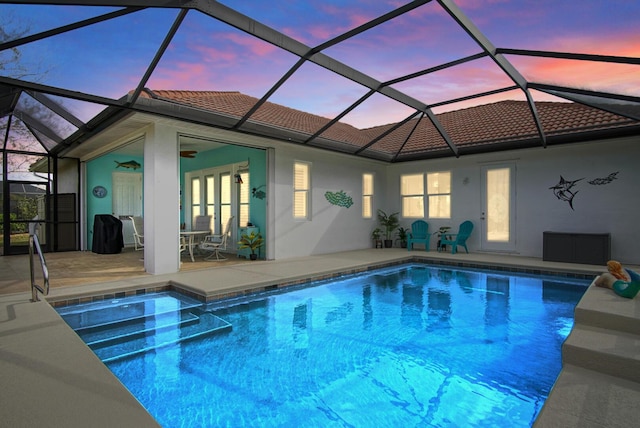 pool at dusk featuring a patio, a lanai, and ceiling fan