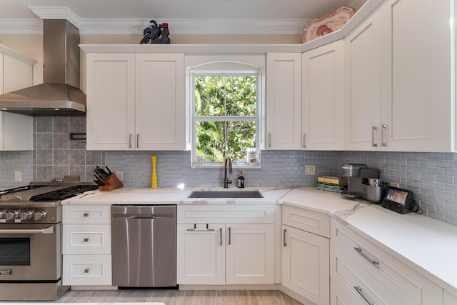 kitchen with sink, white cabinetry, crown molding, appliances with stainless steel finishes, and wall chimney range hood