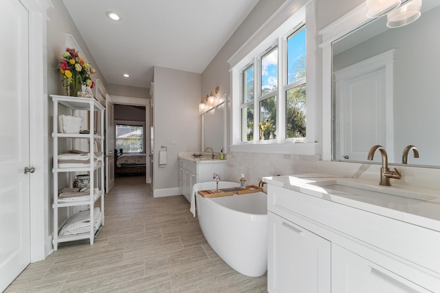 ensuite bathroom with a healthy amount of sunlight, a freestanding tub, two vanities, and a sink
