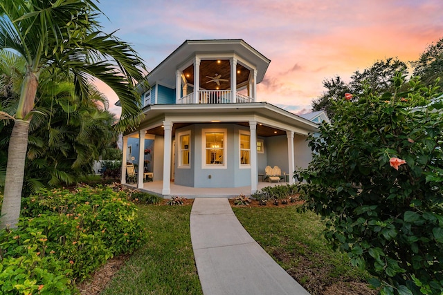 view of front of home with stucco siding, a porch, a ceiling fan, a balcony, and a front lawn