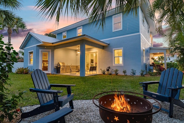 back of property with a patio area, an outdoor fire pit, stucco siding, and a yard