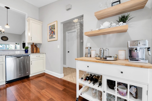 kitchen featuring dark wood-type flooring, an inviting chandelier, wooden counters, stainless steel dishwasher, and pendant lighting