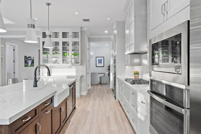 kitchen with a sink, visible vents, an island with sink, glass insert cabinets, and crown molding