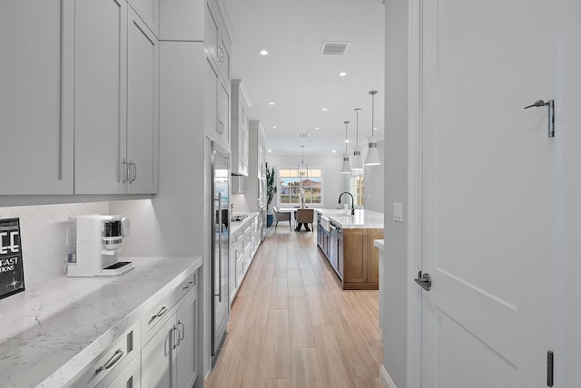 kitchen with visible vents, decorative backsplash, light wood-style flooring, light stone countertops, and recessed lighting