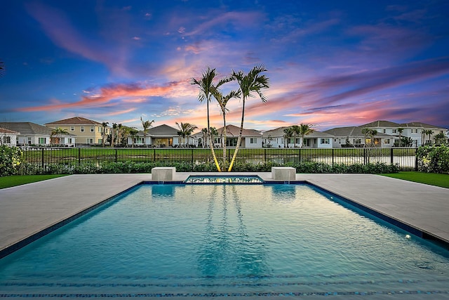 pool at dusk with pool water feature, a jacuzzi, and a patio area