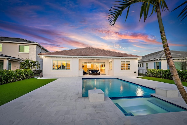 pool at dusk with an outdoor hangout area, a patio, fence, and a pool with connected hot tub