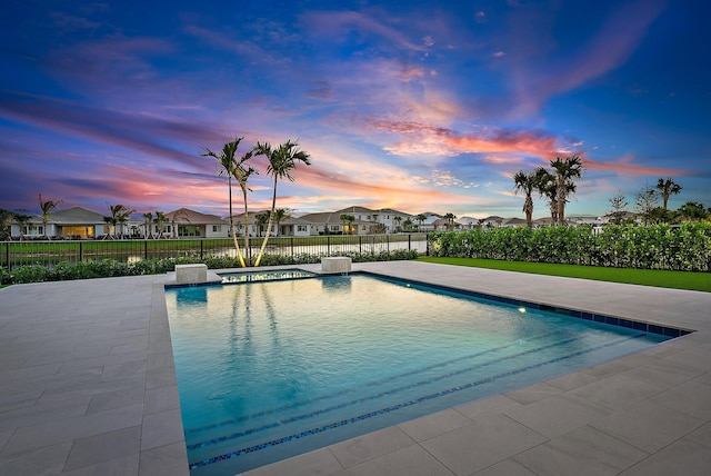 pool at dusk featuring a fenced in pool, a residential view, fence, and a patio