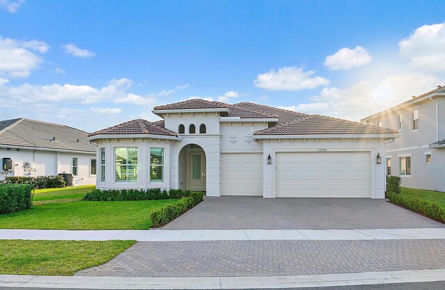 mediterranean / spanish-style house featuring a garage, a tiled roof, decorative driveway, and a front yard