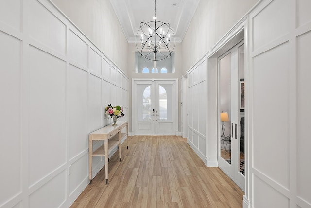 entryway featuring ornamental molding, french doors, light wood-type flooring, a decorative wall, and a notable chandelier