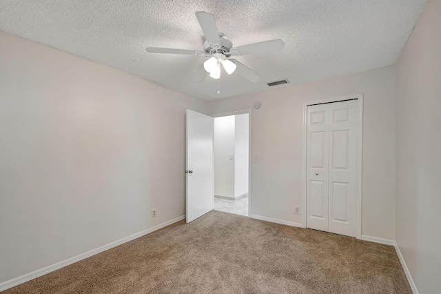 unfurnished bedroom with ceiling fan, light carpet, a textured ceiling, and a closet