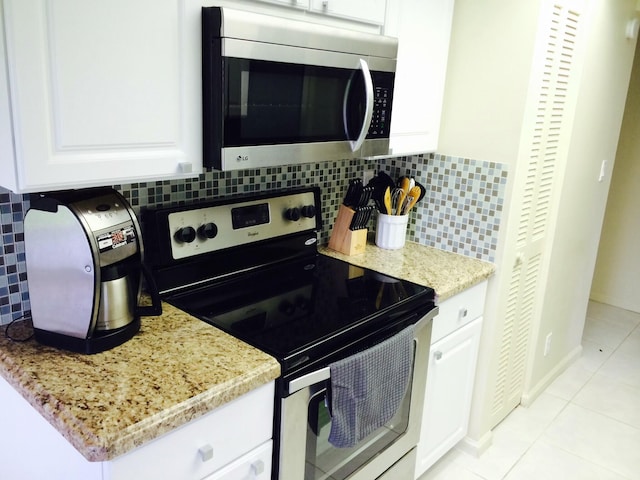 kitchen with white cabinetry, light tile patterned floors, stainless steel appliances, light stone countertops, and backsplash