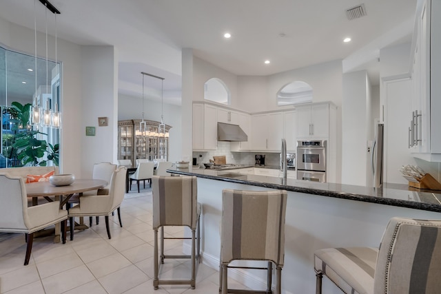 kitchen featuring white cabinetry, an inviting chandelier, a kitchen bar, decorative light fixtures, and dark stone counters