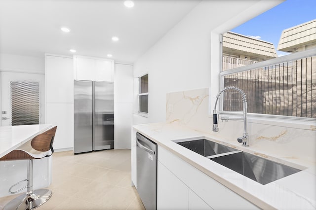 kitchen with sink, white cabinetry, light tile patterned floors, stainless steel appliances, and backsplash