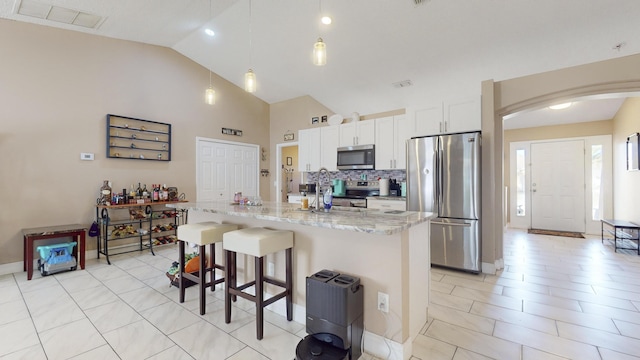 kitchen with white cabinetry, a breakfast bar area, stainless steel appliances, light stone countertops, and a center island with sink