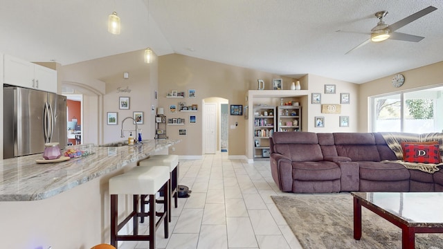 living room with ceiling fan, lofted ceiling, sink, and light tile patterned floors