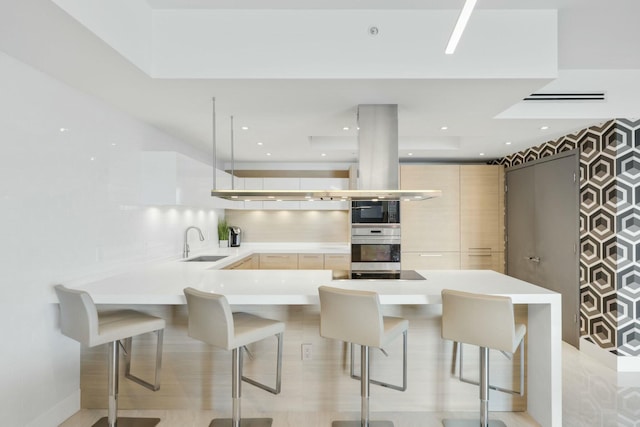 kitchen featuring light brown cabinets, a peninsula, a sink, light countertops, and a kitchen breakfast bar