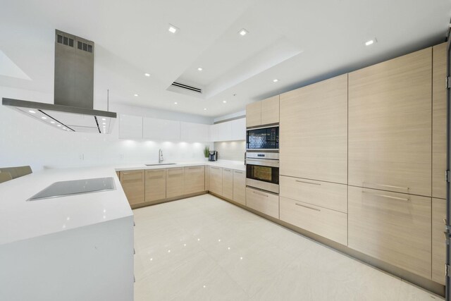 kitchen with a breakfast bar, kitchen peninsula, light brown cabinetry, sink, and black appliances