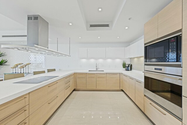 kitchen featuring sink, light brown cabinets, a raised ceiling, island exhaust hood, and black appliances