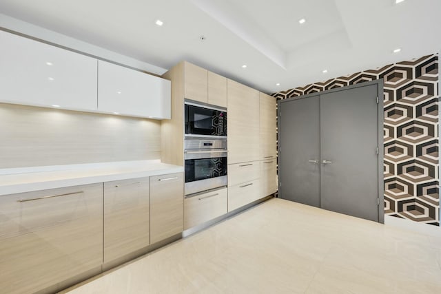 kitchen featuring built in microwave, light brown cabinetry, oven, light countertops, and modern cabinets