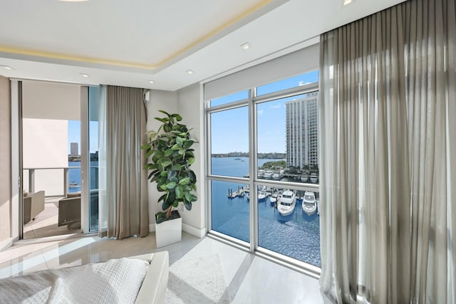 bedroom with a tray ceiling, recessed lighting, a water view, and expansive windows