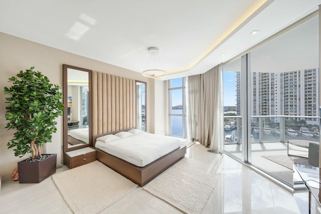 bedroom with access to exterior, floor to ceiling windows, a raised ceiling, and a water view