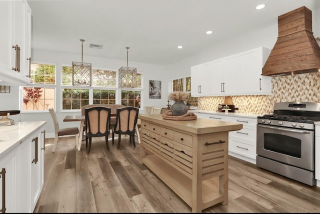 kitchen with premium range hood, stainless steel range with gas cooktop, white cabinets, and decorative light fixtures