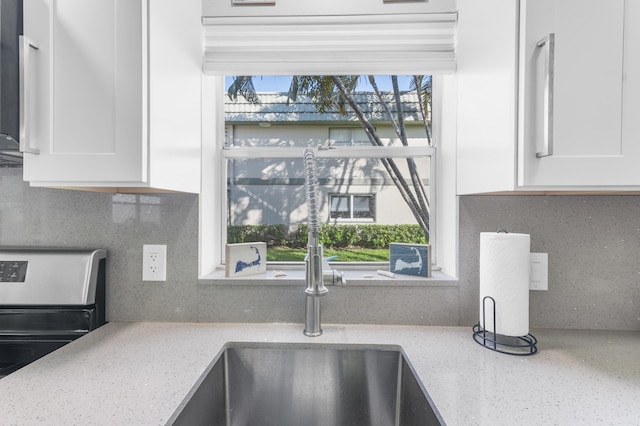 details with electric range, backsplash, light stone countertops, and white cabinets