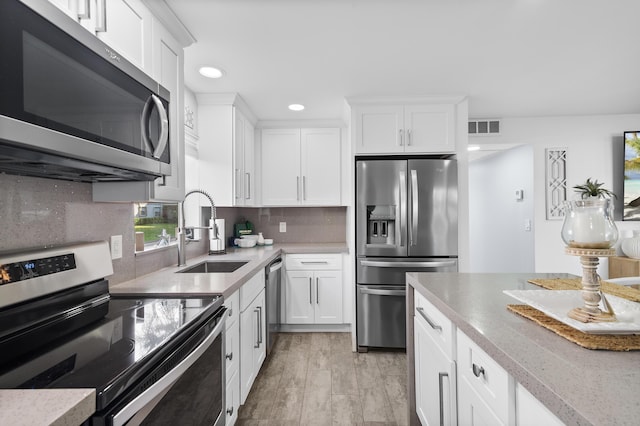 kitchen featuring stainless steel appliances, a sink, visible vents, white cabinetry, and backsplash