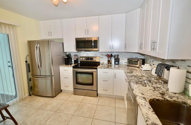 kitchen featuring light stone counters, appliances with stainless steel finishes, decorative backsplash, and white cabinets