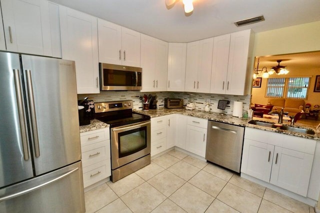 kitchen with sink, stainless steel appliances, light stone counters, white cabinets, and decorative backsplash