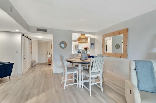 dining area with a barn door and light hardwood / wood-style floors